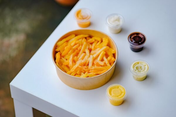 A tempting bowl of crispy french fries with various dips on a white table.