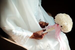 pexels photo 5912573 5912573 A bride with intricate henna designs holds a white flower bouquet with pink ribbons, showcasing elegance and tradition.